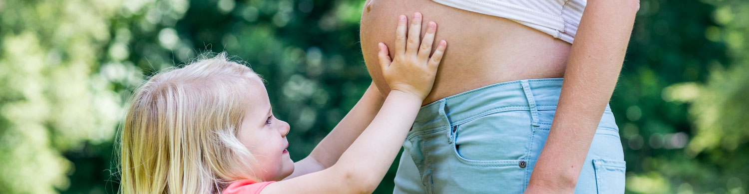 A child places their hand on the belly of an adult.