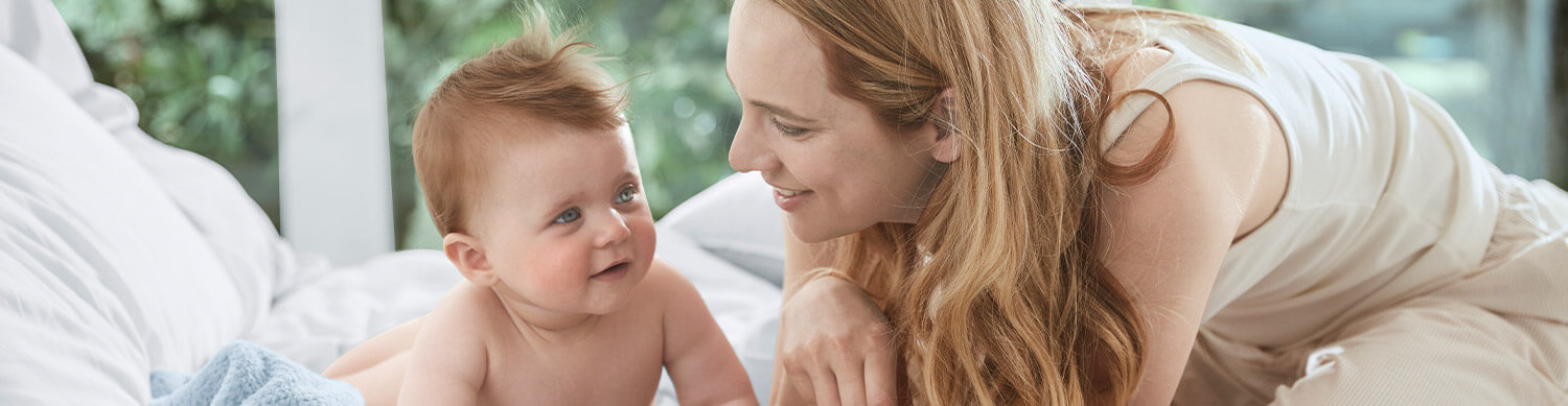 A woman and a baby are lying on a bed, looking at each other.