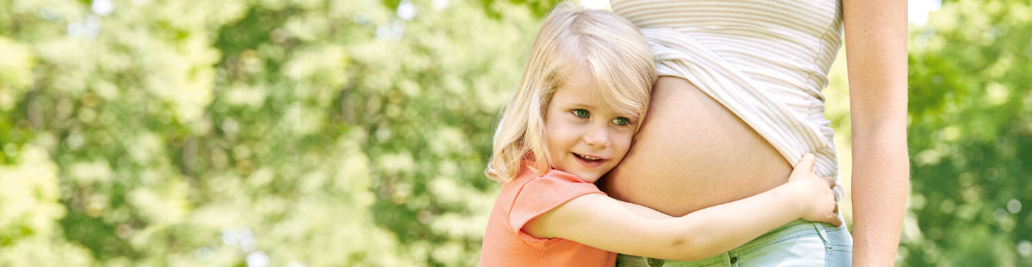 A young child embraces a pregnant woman outdoors.