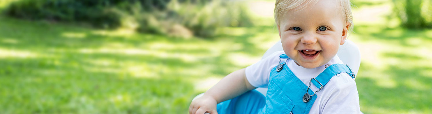 A baby in blue overalls is sitting outdoors.