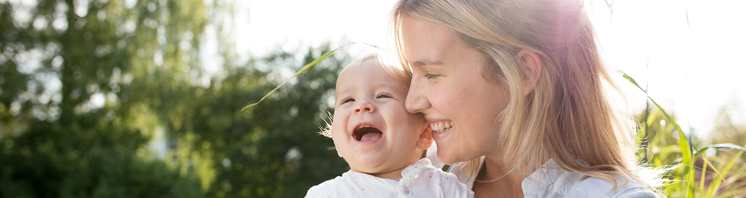 A woman and a baby are outdoors, with the woman holding the baby close to her face, and the baby is looking up at her.