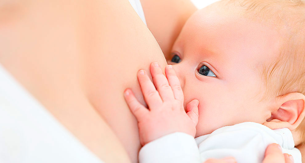 A close-up of a baby's face, with one eye visible, as the baby nurses from a woman's breast.