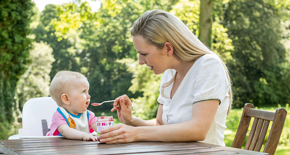 A woman feeds a baby outdoors.