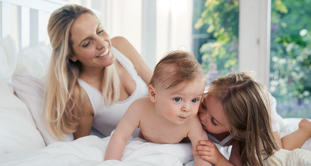 A woman and two children are engaged in a playful interaction on a bed.