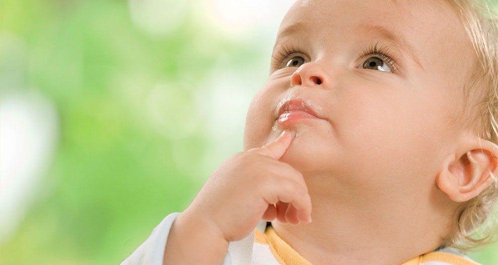 A baby with a finger in the mouth, looking up.