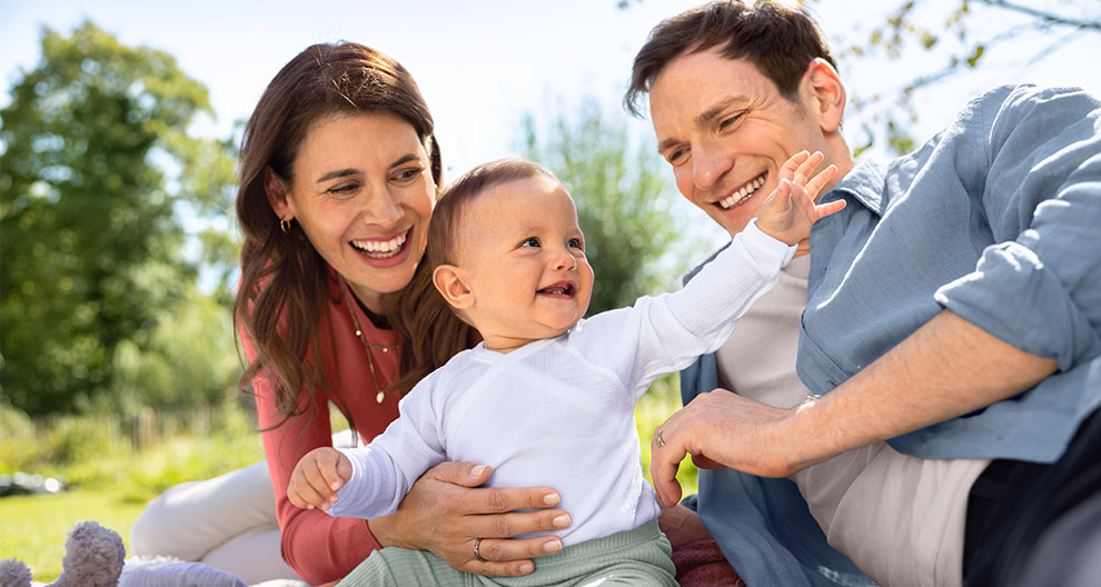 A man, a woman, and a baby are outdoors, with the man and woman interacting with the baby.