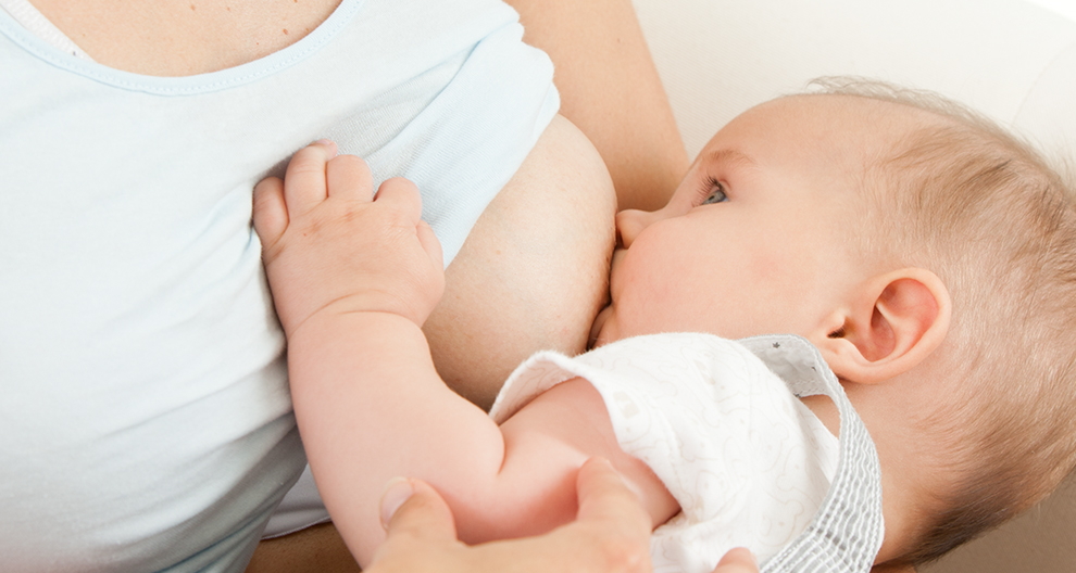 Primer plano de la cara de un bebé, con un ojo visible, mientras mama del pecho de una mujer.
